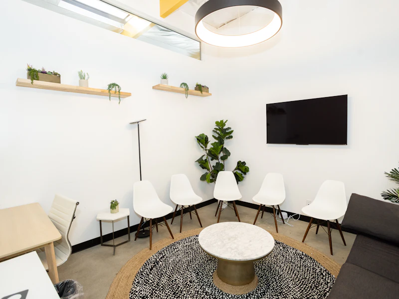 Sala de espera clara, com cadeiras, plantas e tapete redondo