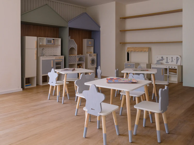 Sala infantil com mesinhas, cadeiras baixas e brinquedos de madeira