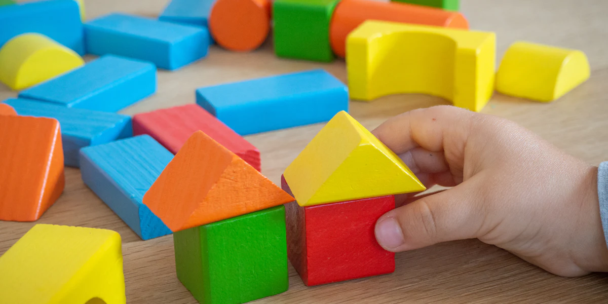 Mão de criança montando uma construção com blocos de madeira coloridos