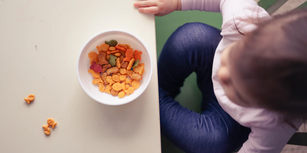 Vista de cima de uma criança em cadeira de alimentação diante de uma tigela com comida colorida