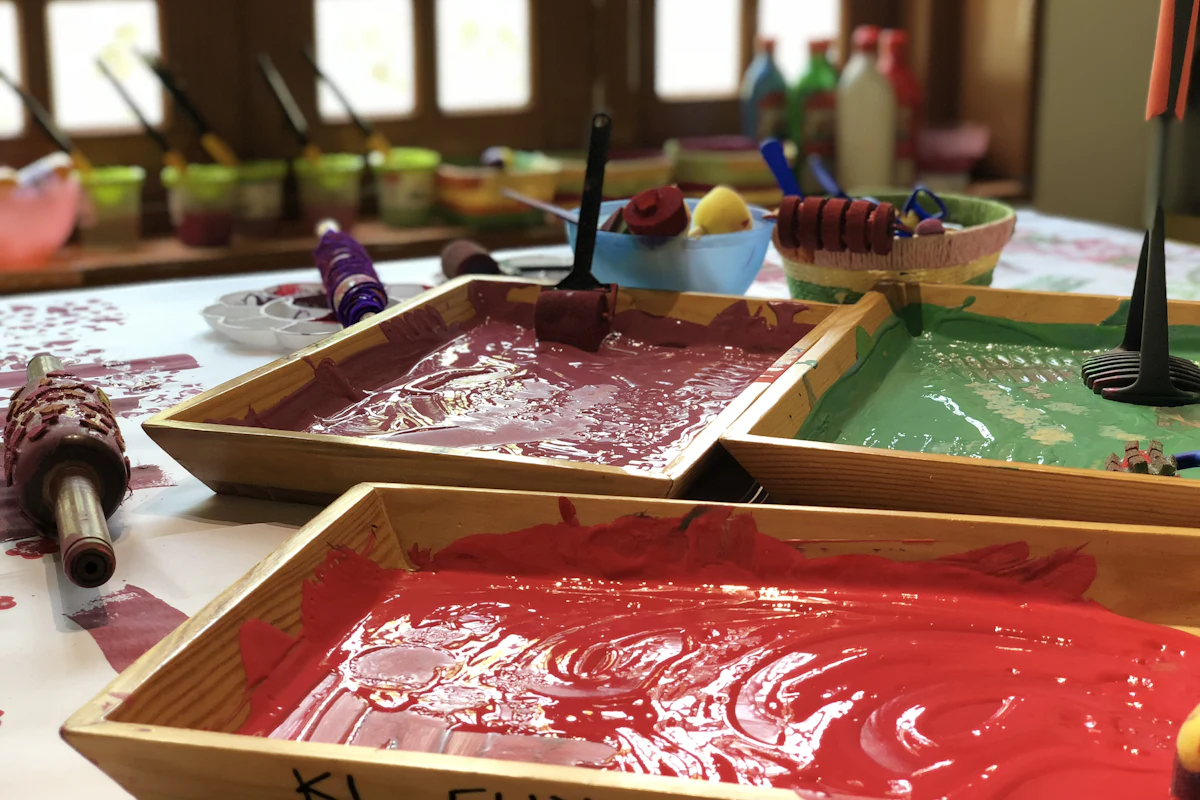 Bandejas de tinta guache em tons quentes sobre uma mesa de ateliê