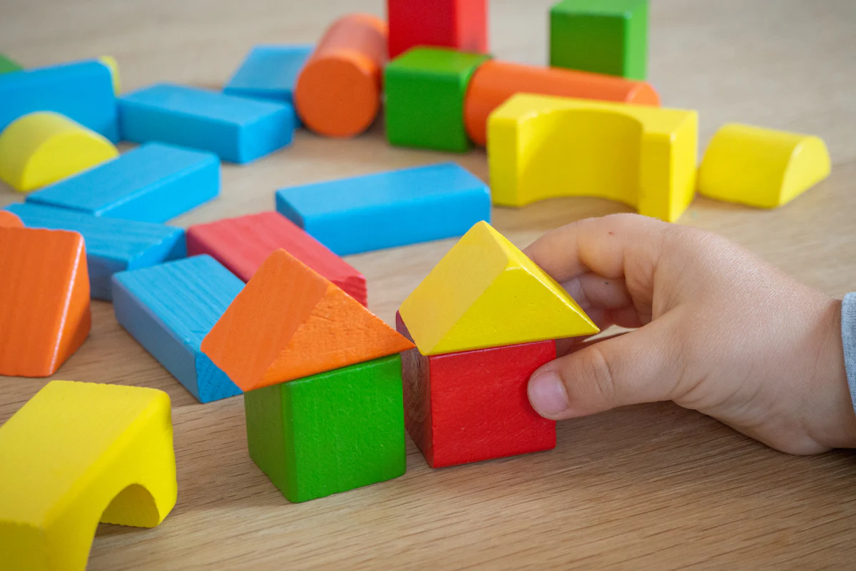 Mão de criança montando uma construção com blocos de madeira coloridos