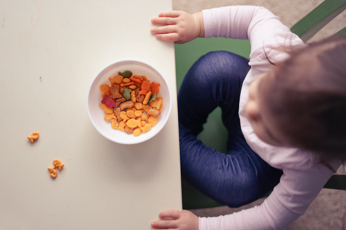 Vista de cima de uma criança em cadeira de alimentação diante de uma tigela com comida colorida