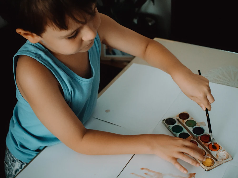 Criança pintando com aquarela em uma mesa clara